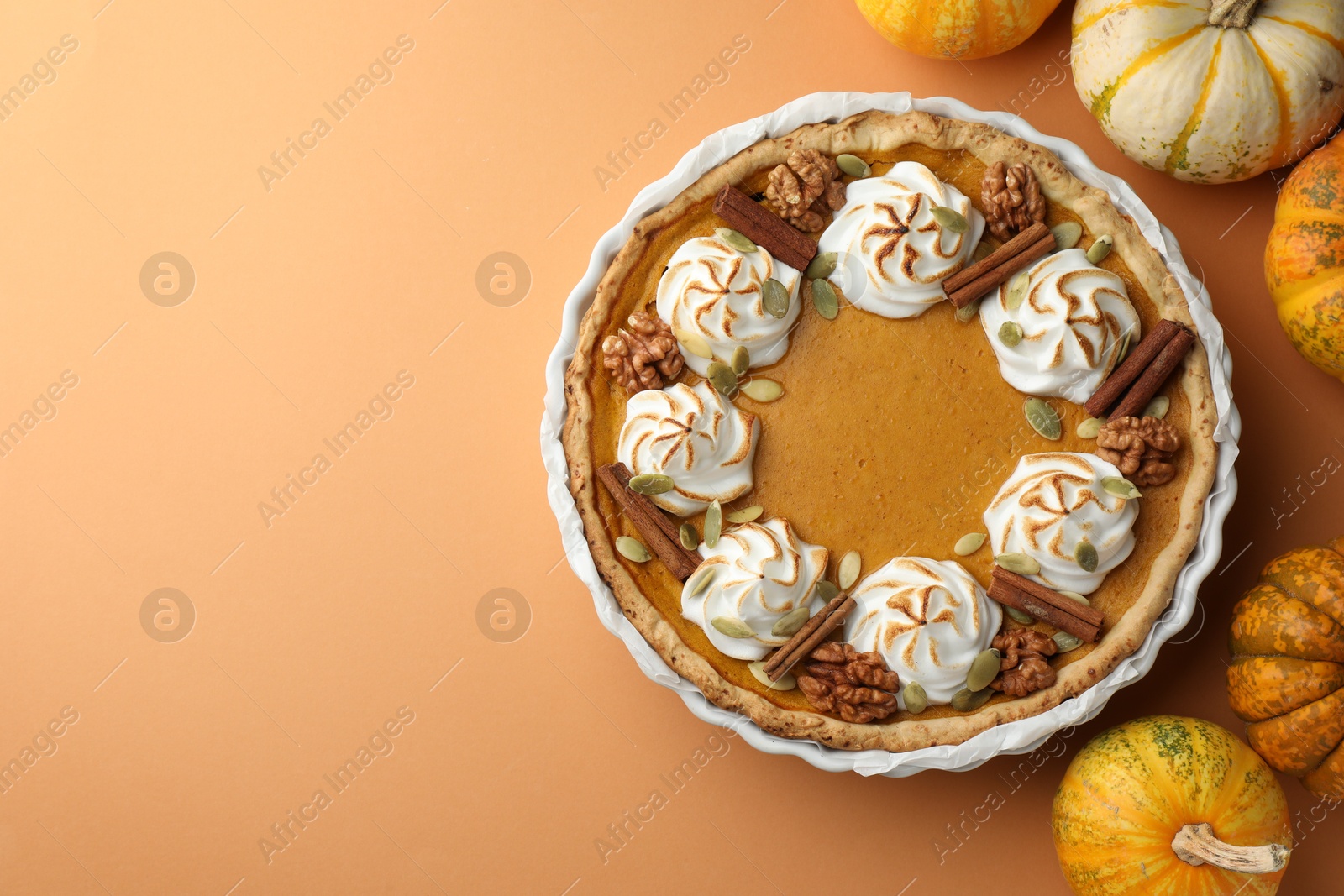 Photo of Delicious homemade pumpkin pie in baking dish and fresh pumpkins on orange table, flat lay. Space for text