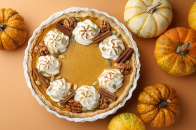 Delicious homemade pumpkin pie in baking dish and fresh pumpkins on orange table, flat lay