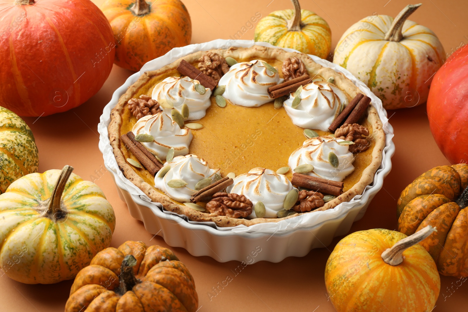 Photo of Delicious homemade pumpkin pie in baking dish and fresh pumpkins on orange table, closeup