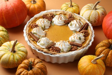 Photo of Delicious homemade pumpkin pie in baking dish and fresh pumpkins on orange table, closeup