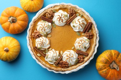 Delicious homemade pumpkin pie in baking dish and fresh pumpkins on light blue table, flat lay