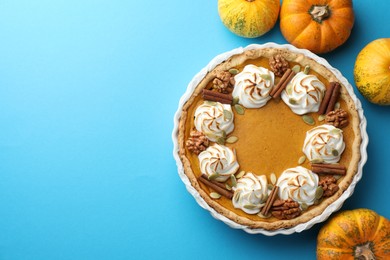 Photo of Delicious homemade pumpkin pie in baking dish and fresh pumpkins on light blue table, flat lay. Space for text