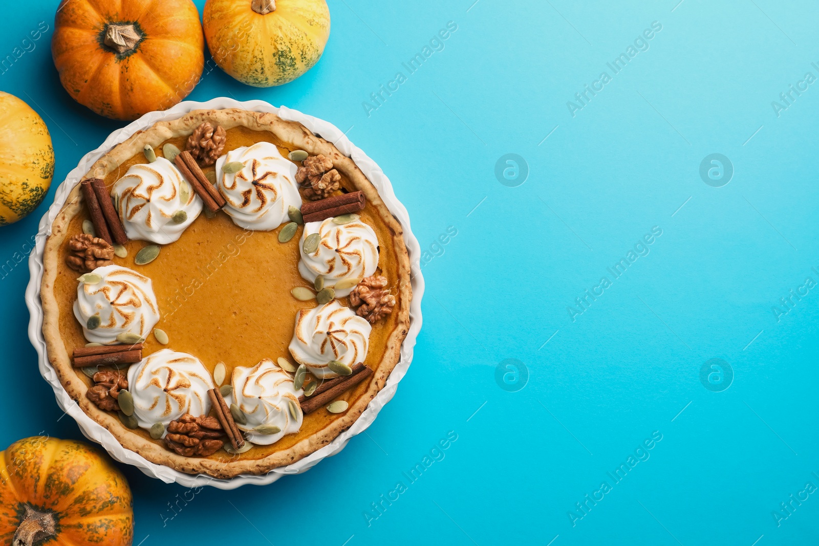 Photo of Delicious homemade pumpkin pie in baking dish and fresh pumpkins on light blue table, flat lay. Space for text