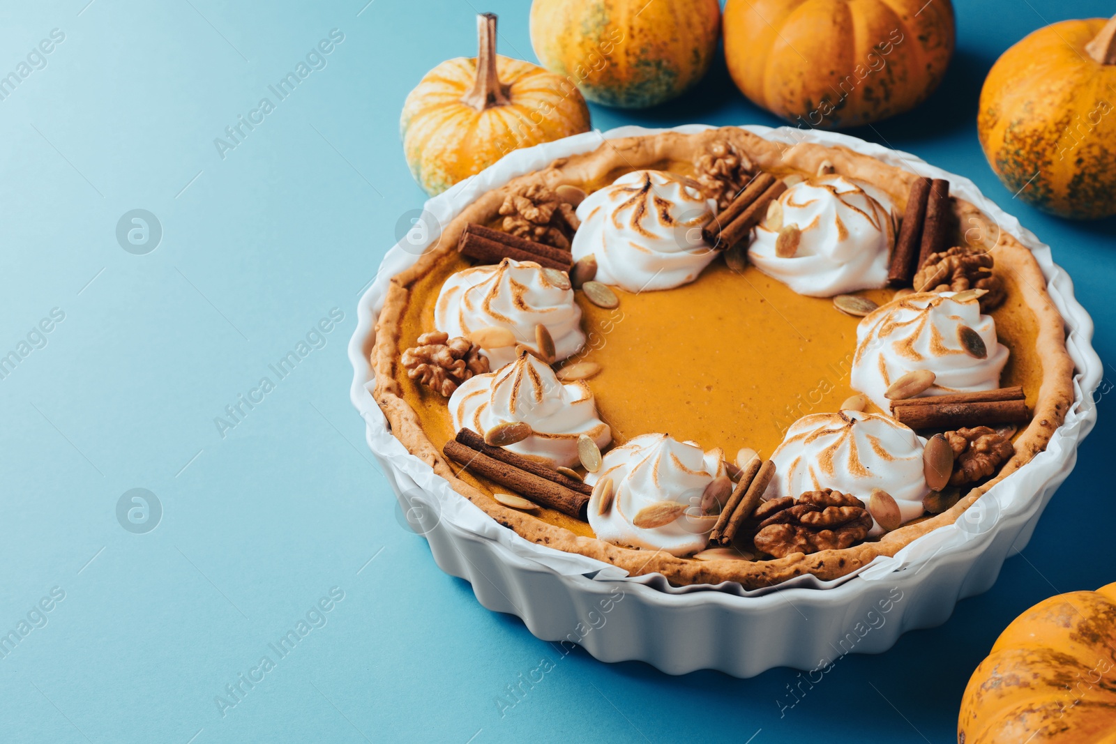 Photo of Delicious homemade pumpkin pie in baking dish and fresh pumpkins on light blue table, closeup. Space for text