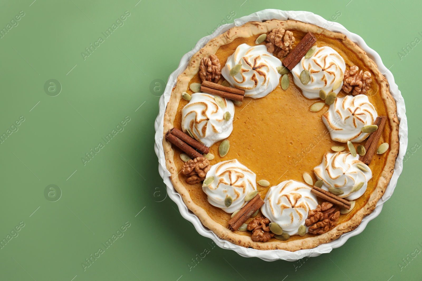 Photo of Tasty homemade pumpkin pie in baking dish on green table, top view. Space for text