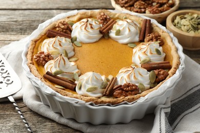 Tasty homemade pumpkin pie in baking dish and cake server on wooden table, closeup