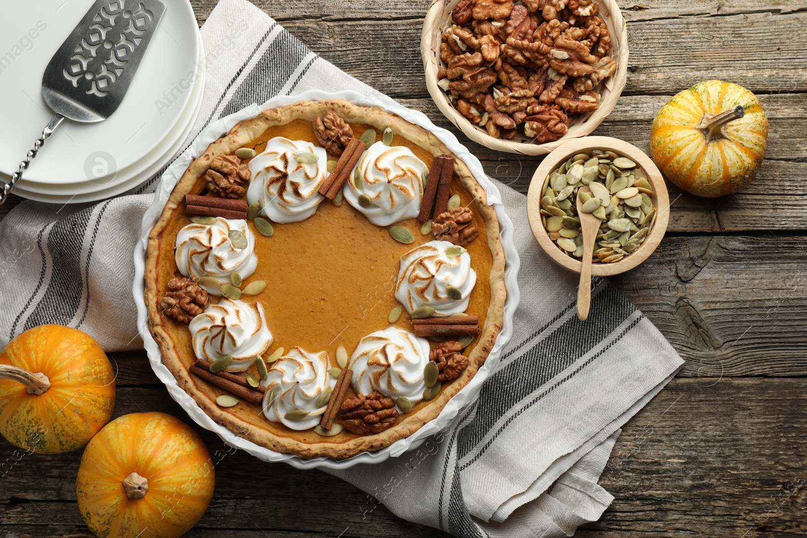 Photo of Tasty homemade pumpkin pie in baking dish and ingredients on wooden table, flat lay