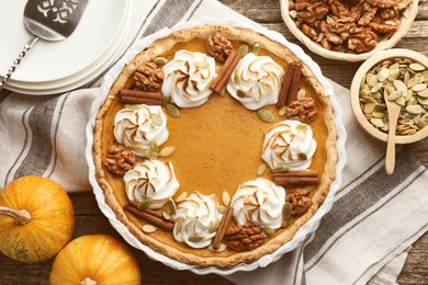 Tasty homemade pumpkin pie in baking dish and ingredients on wooden table, flat lay