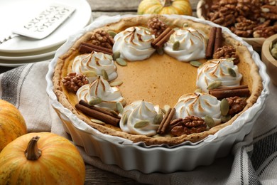 Tasty homemade pumpkin pie in baking dish and ingredients on wooden table, closeup