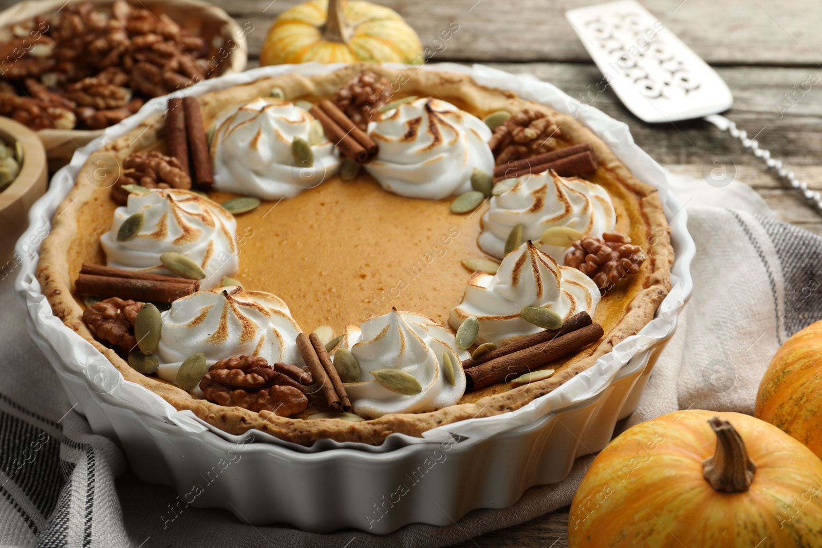 Photo of Tasty homemade pumpkin pie in baking dish and ingredients on wooden table, closeup