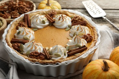 Tasty homemade pumpkin pie in baking dish and ingredients on wooden table, closeup