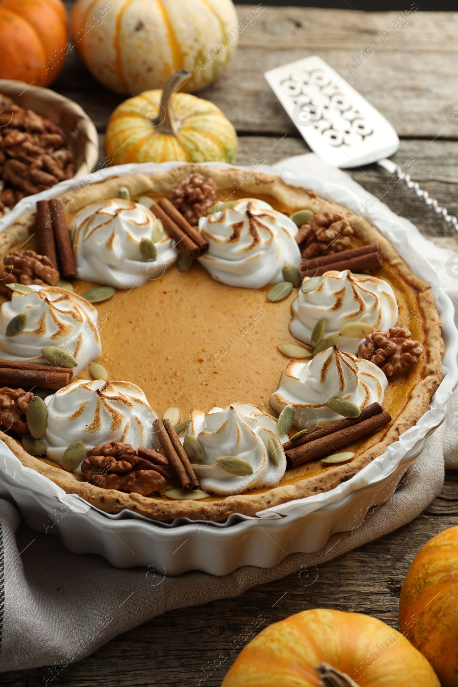 Photo of Tasty homemade pumpkin pie, ingredients and cake server on wooden table, closeup