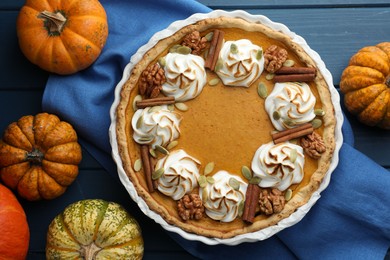 Delicious homemade pumpkin pie in baking dish and fresh pumpkins on blue wooden table, flat lay