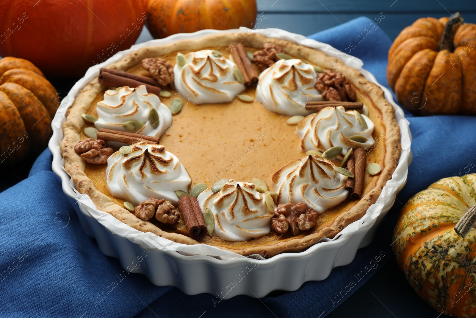 Photo of Delicious homemade pumpkin pie in baking dish and fresh pumpkins on blue table, closeup