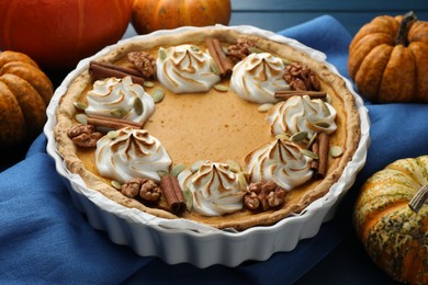 Photo of Delicious homemade pumpkin pie in baking dish and fresh pumpkins on blue table, closeup