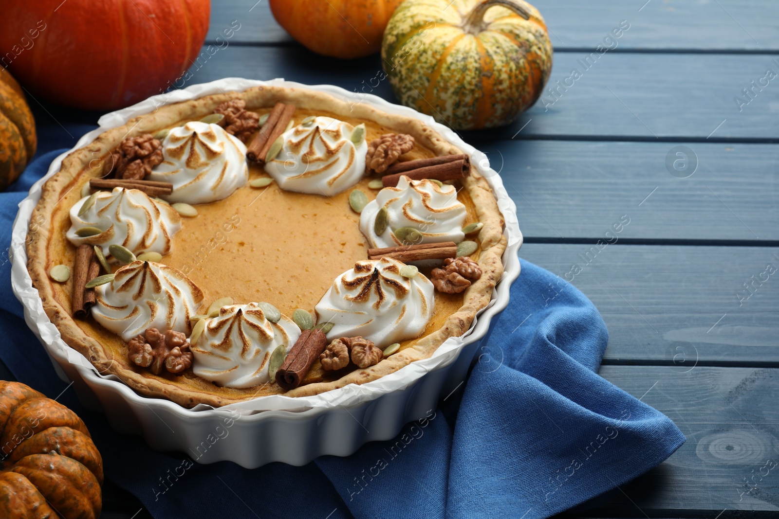 Photo of Delicious homemade pumpkin pie in baking dish and fresh pumpkins on blue wooden table, closeup. Space for text