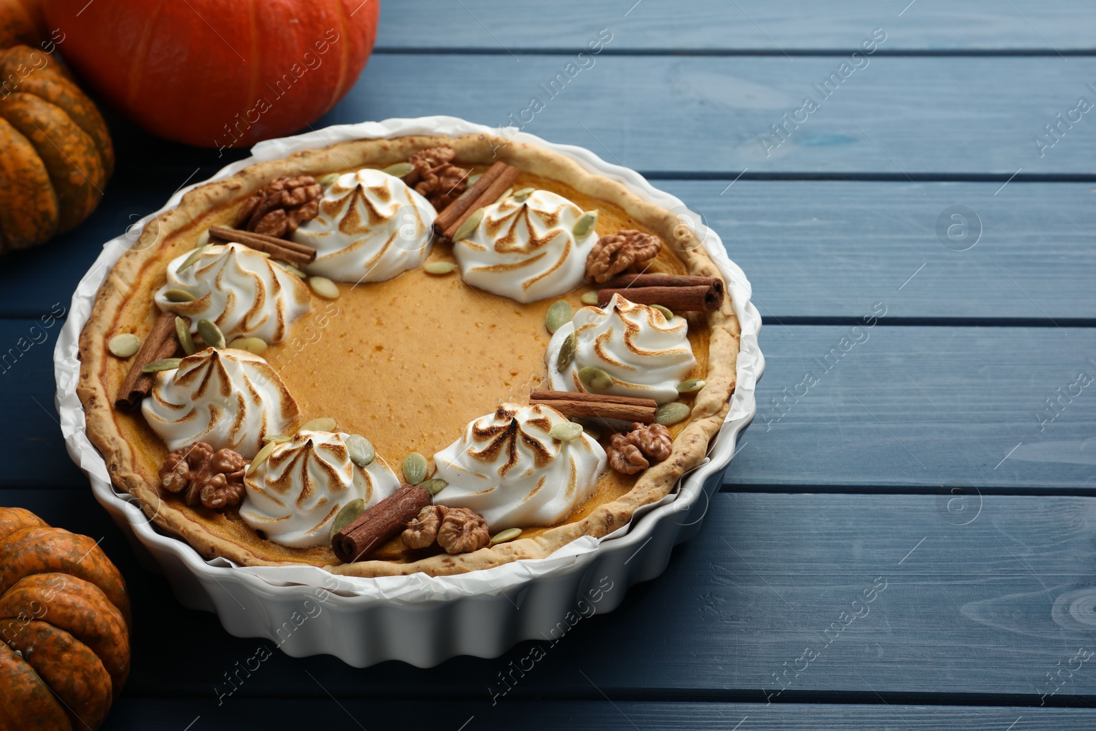 Photo of Delicious homemade pumpkin pie in baking dish and fresh pumpkins on blue wooden table, closeup. Space for text