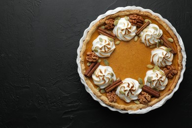 Delicious homemade pumpkin pie in baking dish on black textured table, top view. Space for text