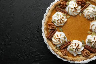 Delicious homemade pumpkin pie in baking dish on black textured table, top view. Space for text