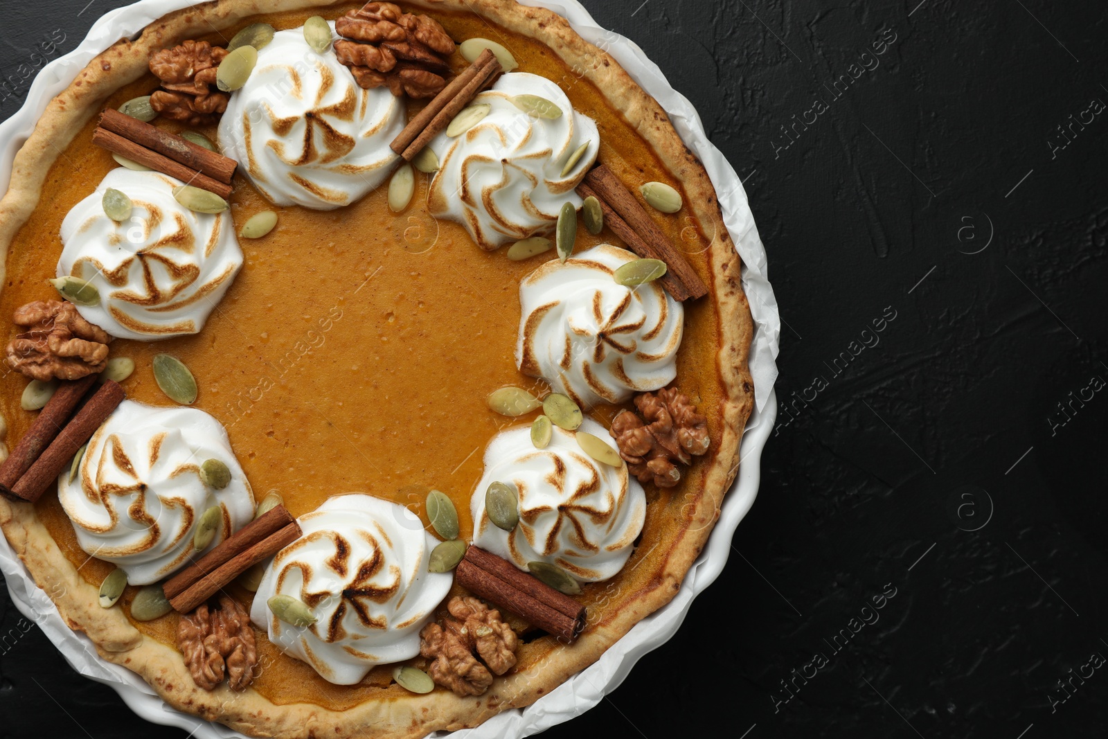 Photo of Delicious homemade pumpkin pie in baking dish on black textured table, top view. Space for text