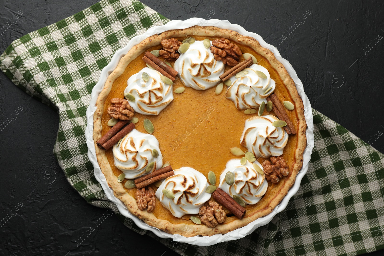 Photo of Delicious homemade pumpkin pie in baking dish on black textured table, top view