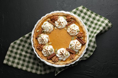 Photo of Delicious homemade pumpkin pie in baking dish on black textured table, top view