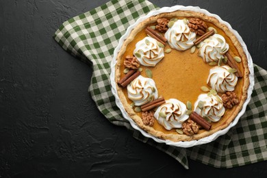 Photo of Delicious homemade pumpkin pie in baking dish on black textured table, top view. Space for text