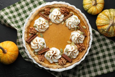 Delicious homemade pumpkin pie in baking dish and fresh pumpkins on black textured table, flat lay