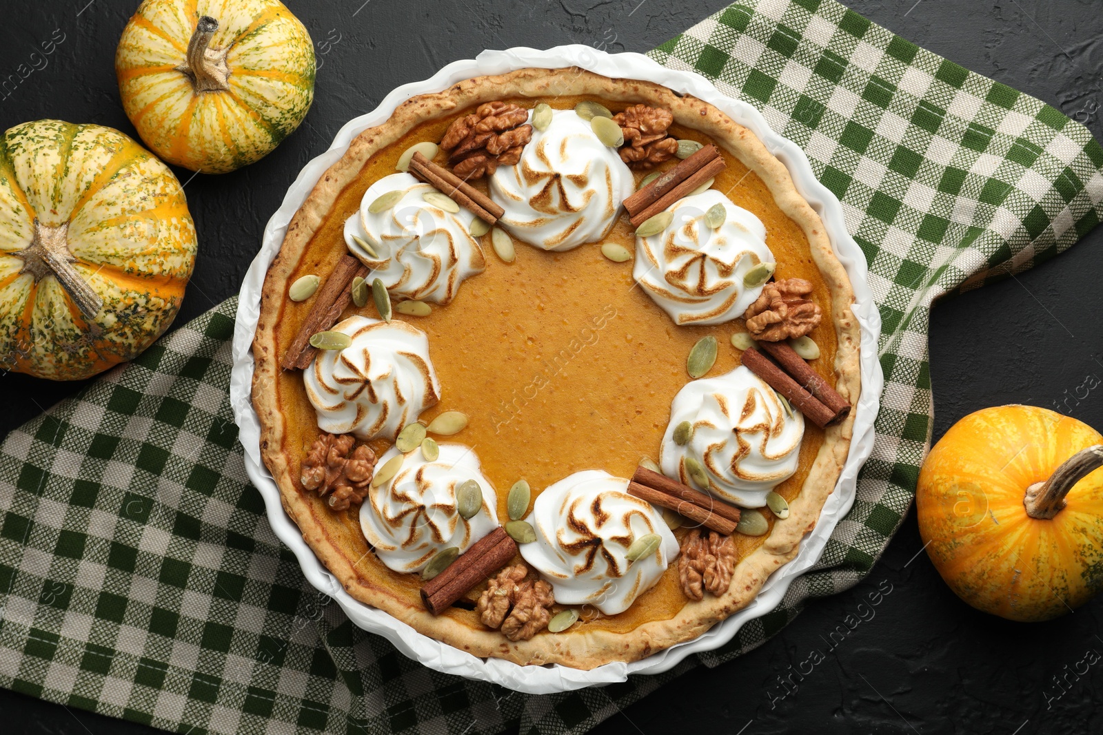 Photo of Delicious homemade pumpkin pie in baking dish and fresh pumpkins on black textured table, flat lay