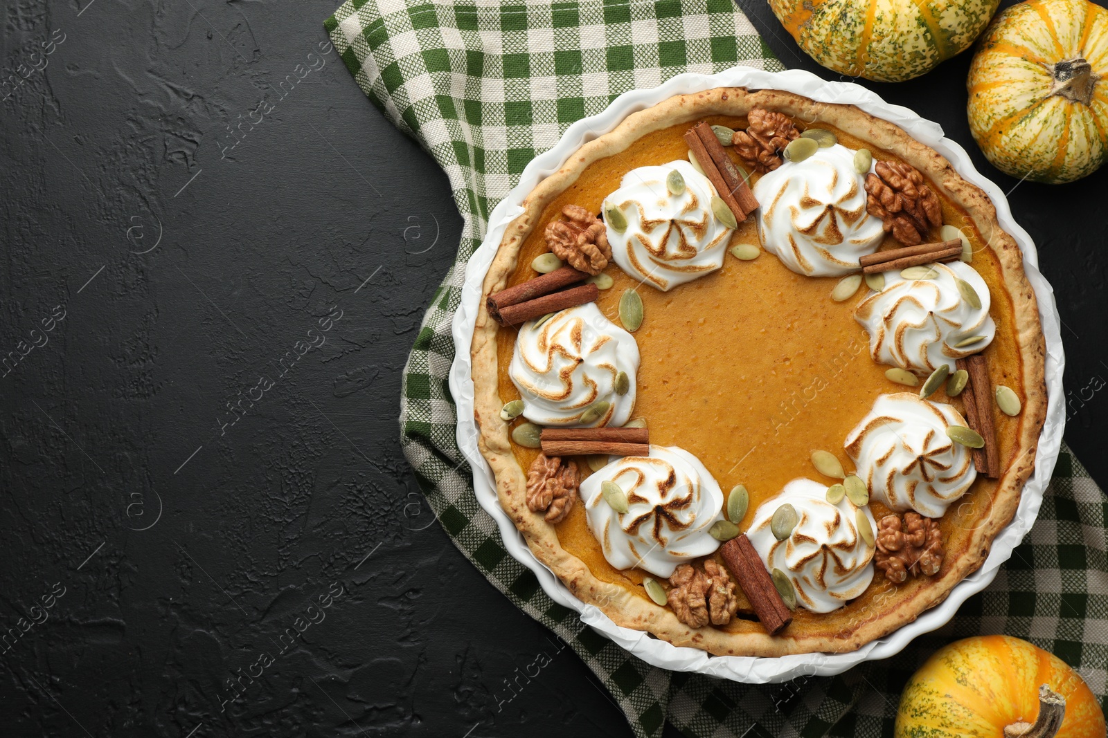 Photo of Delicious homemade pumpkin pie in baking dish and fresh pumpkins on black textured table, flat lay. Space for text