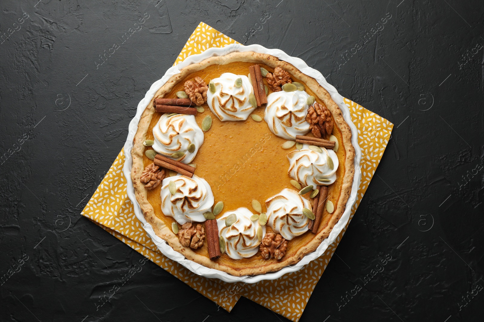 Photo of Delicious homemade pumpkin pie in baking dish on black textured table, top view