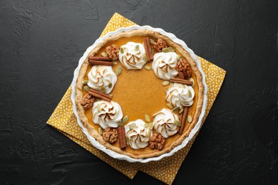 Photo of Delicious homemade pumpkin pie in baking dish on black textured table, top view