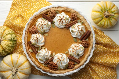 Delicious homemade pumpkin pie in baking dish and fresh pumpkins on white wooden table, flat lay