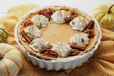 Photo of Delicious homemade pumpkin pie in baking dish and fresh pumpkins on white table, closeup