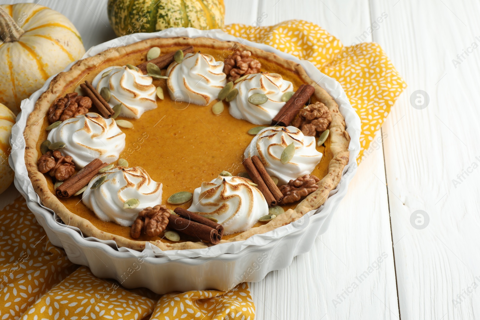 Photo of Delicious homemade pumpkin pie in baking dish and fresh pumpkins on white wooden table, closeup