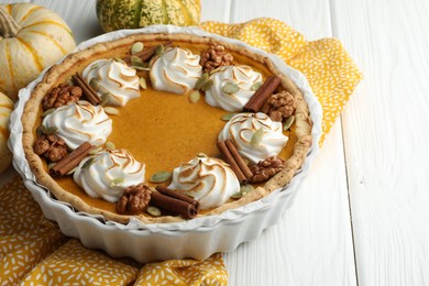 Delicious homemade pumpkin pie in baking dish and fresh pumpkins on white wooden table, closeup