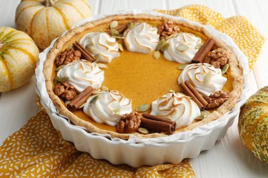 Delicious homemade pumpkin pie in baking dish and fresh pumpkins on white wooden table, closeup