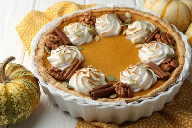 Delicious homemade pumpkin pie in baking dish and fresh pumpkins on white wooden table, closeup