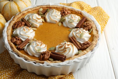 Photo of Delicious homemade pumpkin pie in baking dish and fresh pumpkins on white wooden table, closeup