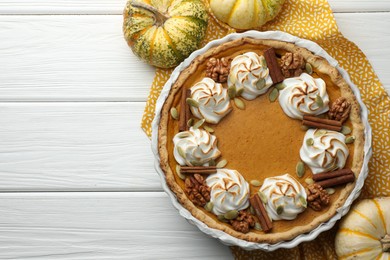 Photo of Delicious homemade pumpkin pie in baking dish and fresh pumpkins on white wooden table, flat lay. Space for text