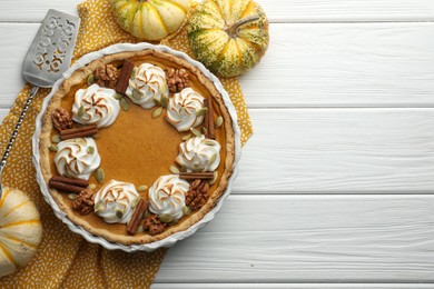 Tasty homemade pumpkin pie in baking dish, fresh pumpkins and cake server on white wooden table, flat lay. Space for text