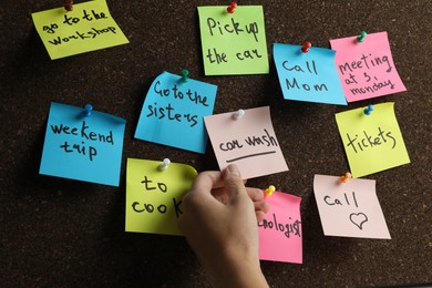 Photo of Woman holding reminder note pinned to cork board, closeup