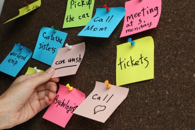 Photo of Woman holding reminder note pinned to cork board, closeup