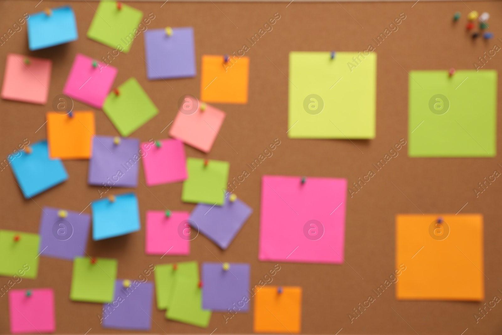 Photo of Blurred view of corkboard filled with colorful notes and pins