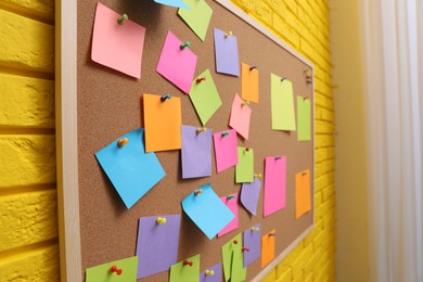 Corkboard filled with colorful notes and pins on yellow brick wall indoors