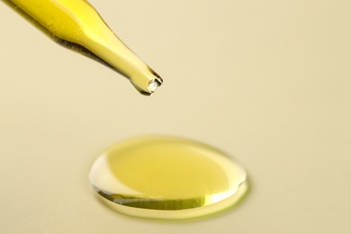 Photo of Cosmetic oil dripping from pipette on dark beige background, closeup. Space for text