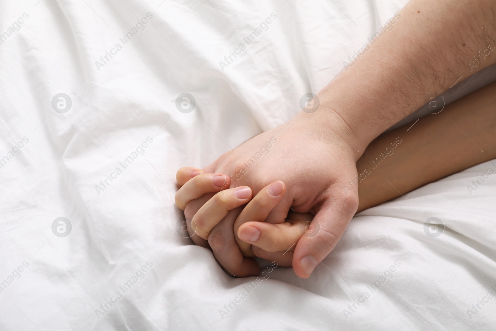 Photo of Lovely couple holding hands in bed, top view. Space for text