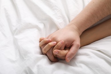 Photo of Lovely couple holding hands in bed, top view. Space for text