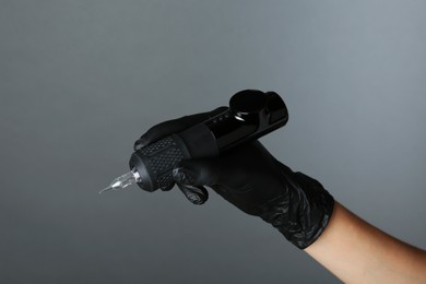 Photo of Professional cosmetologist holding permanent makeup machine on grey background, closeup