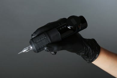 Photo of Professional cosmetologist holding permanent makeup machine on grey background, closeup